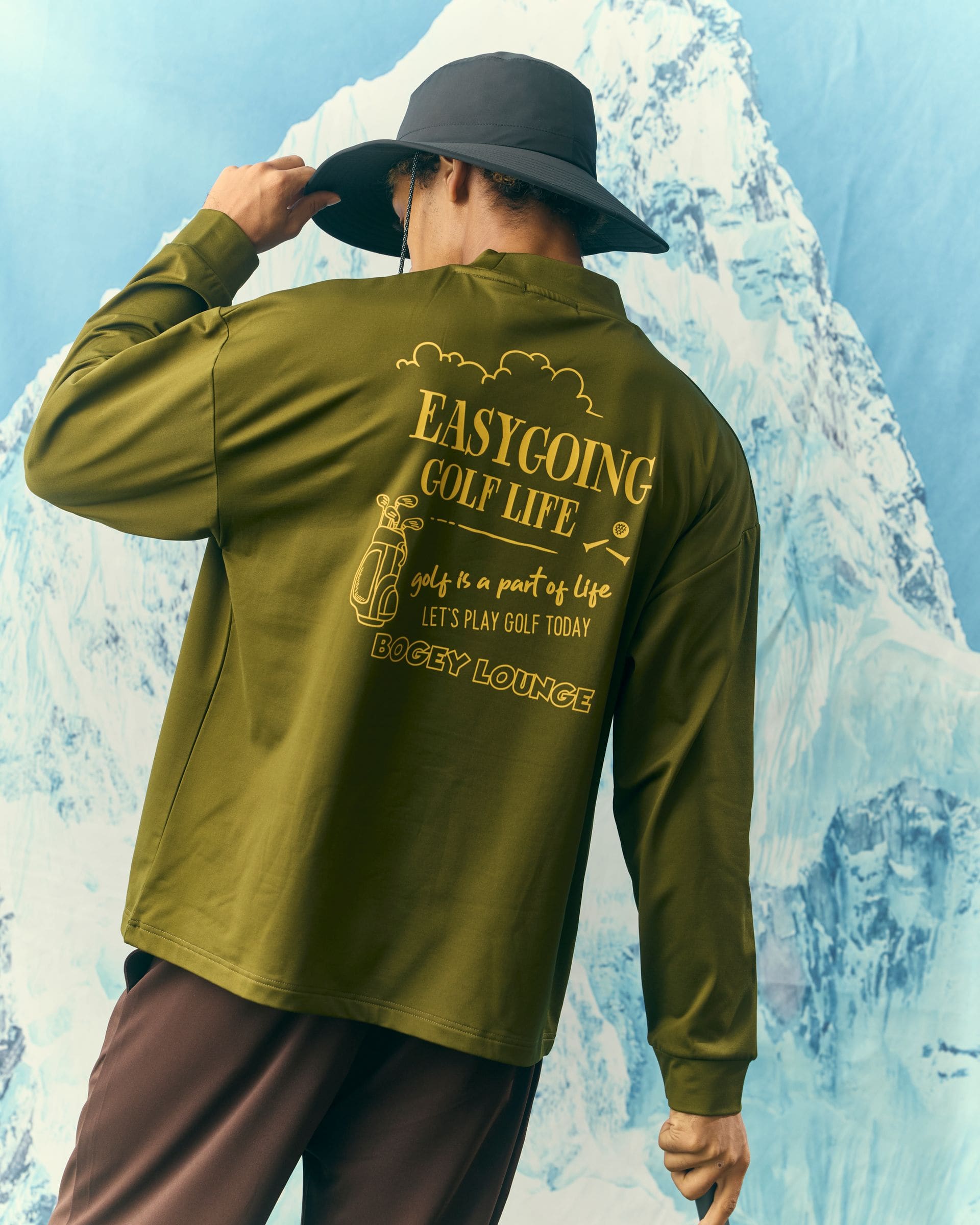 オリーブの長袖の背中にある EASYGOING GOLF LIFE のプリント。つば広の帽子をかぶった後ろ姿